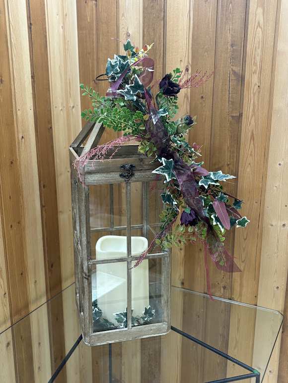 Decorative lantern with faux greenery and dark purple flowers