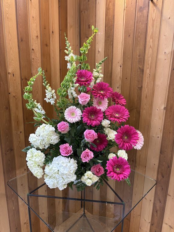 Tall arrangement of hot pink gerberas, pink roses, white hydrangeas, and green bells of Ireland.