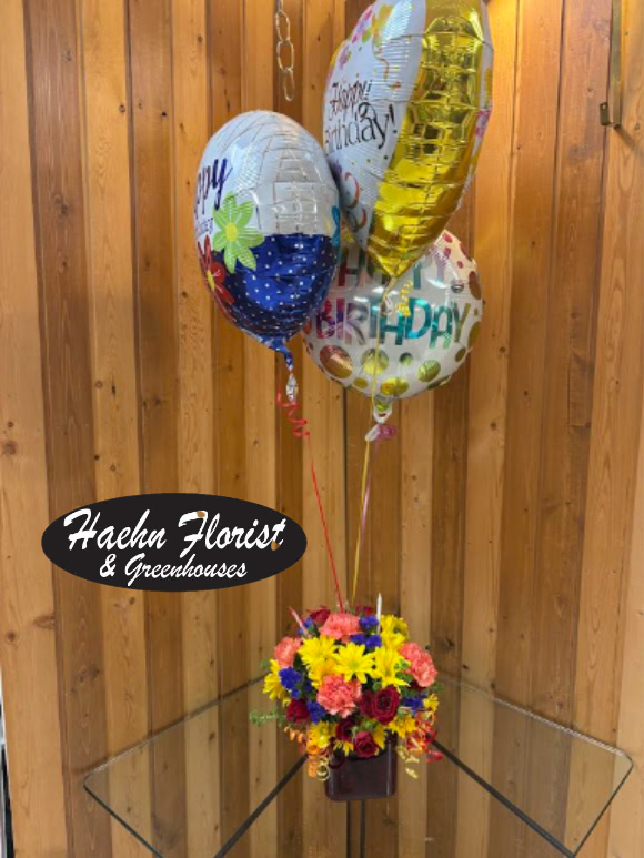 Birthday balloons above a colorful flower arrangement in a vase