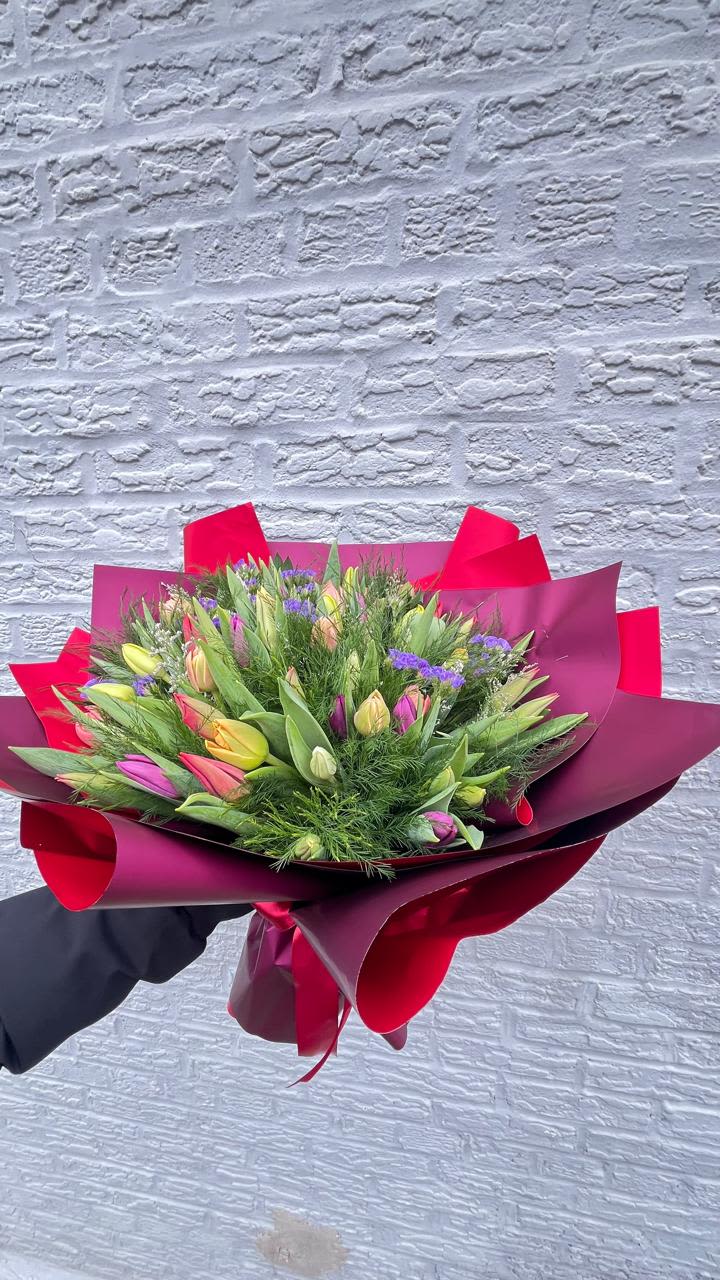 Bouquet of multicolored tulips wrapped in burgundy and pink paper