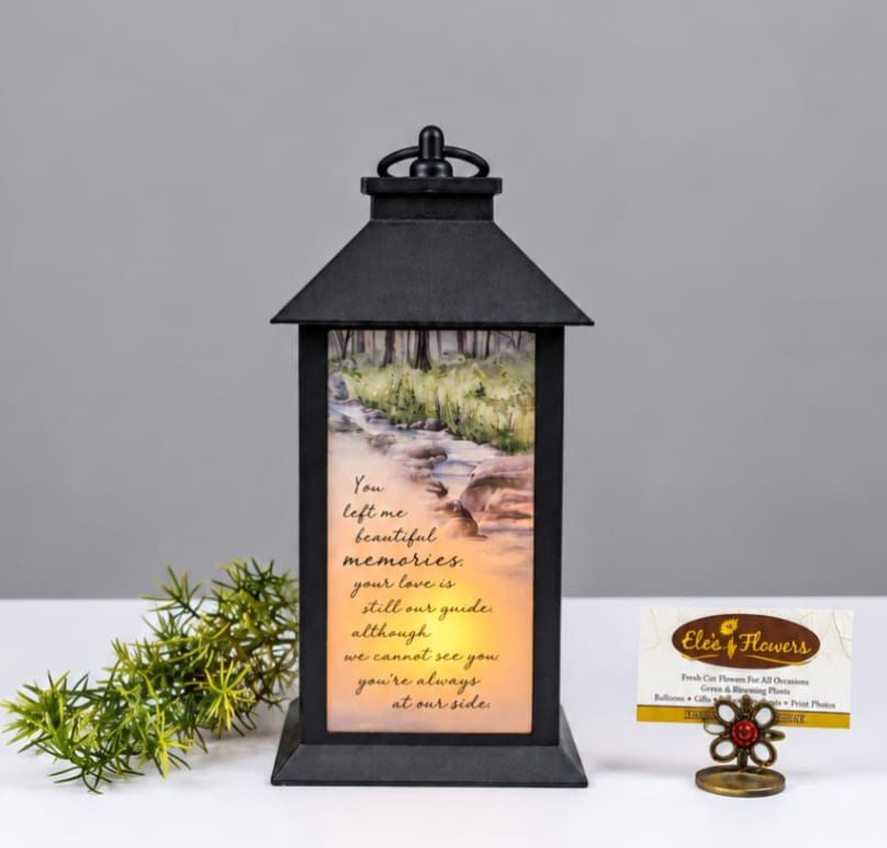 Black lantern with a memorial message and a small greenery sprig beside it