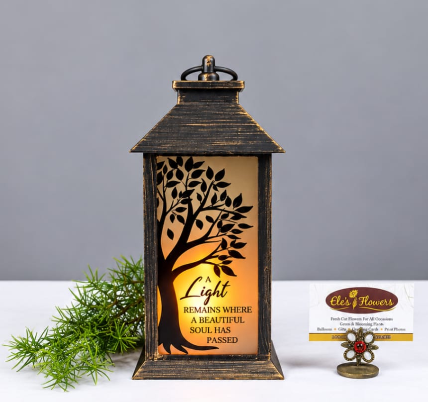 Black lantern with a tree silhouette and memorial text, lit from within