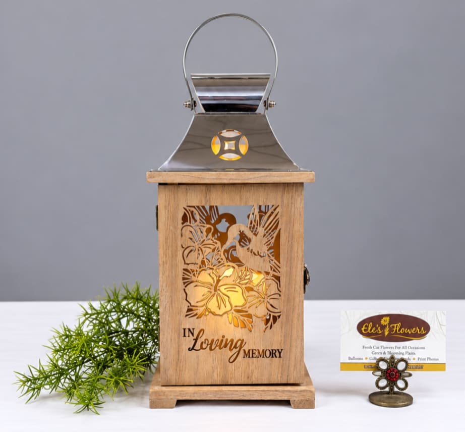 Wooden memorial lantern with metal top and floral cutouts, lit from within