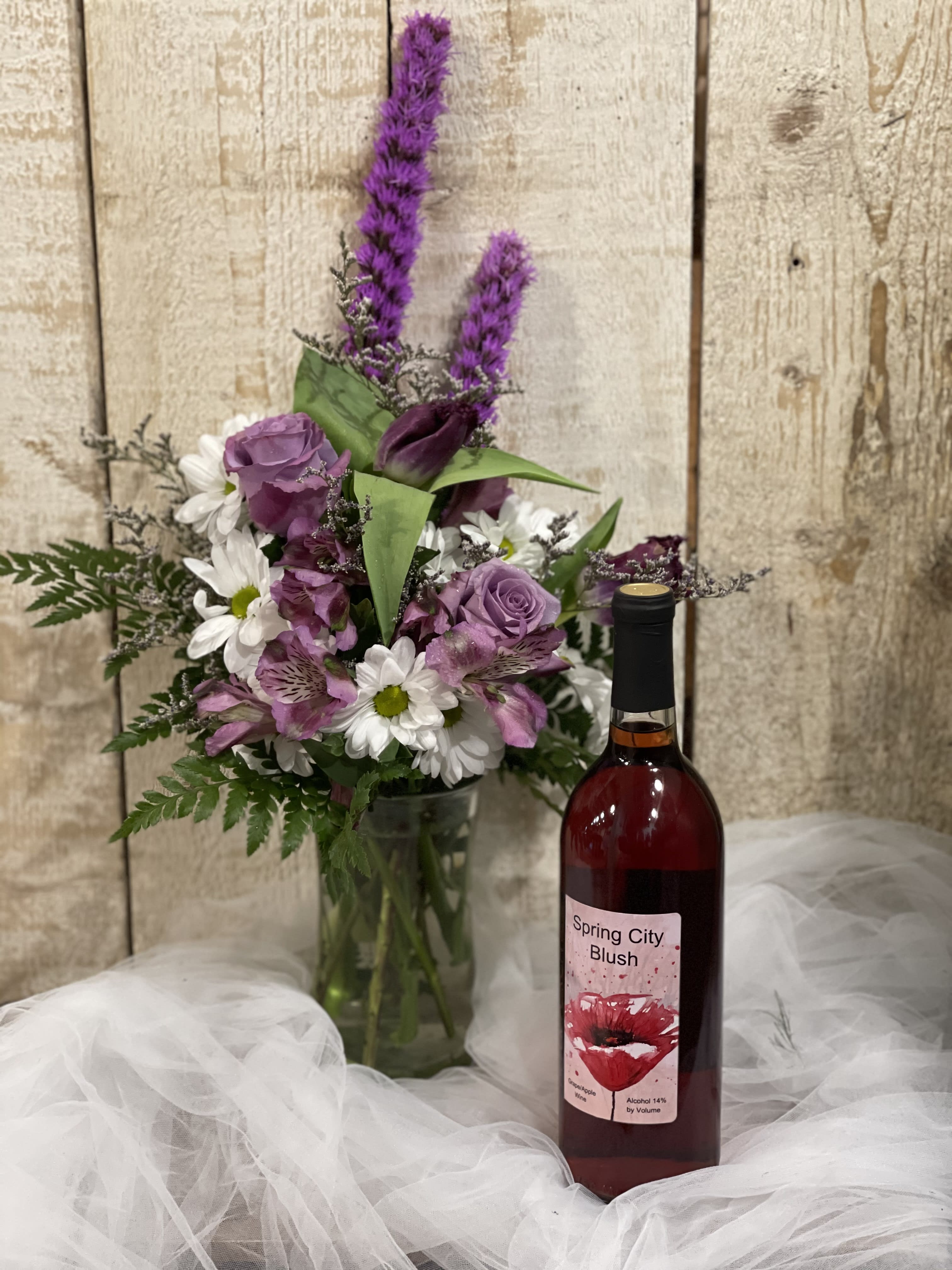 Purple and white bouquet in a glass vase beside a bottle of wine