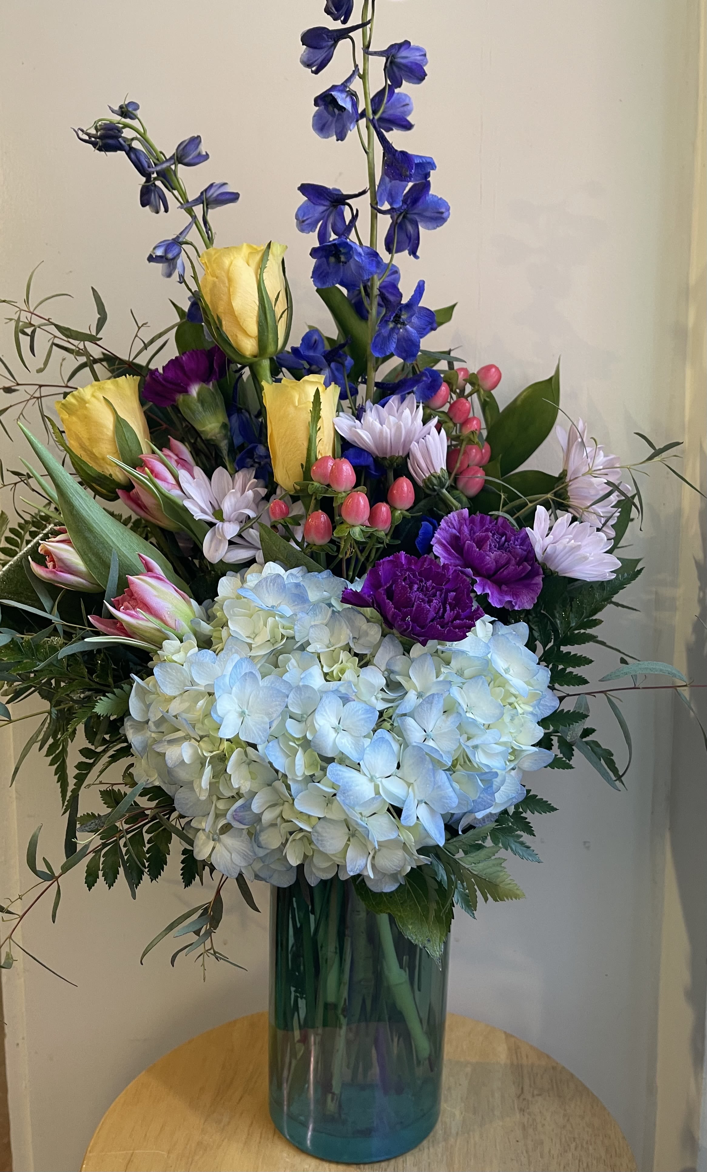 Tall mixed bouquet in a glass vase with blue, yellow, pink, and white flowers