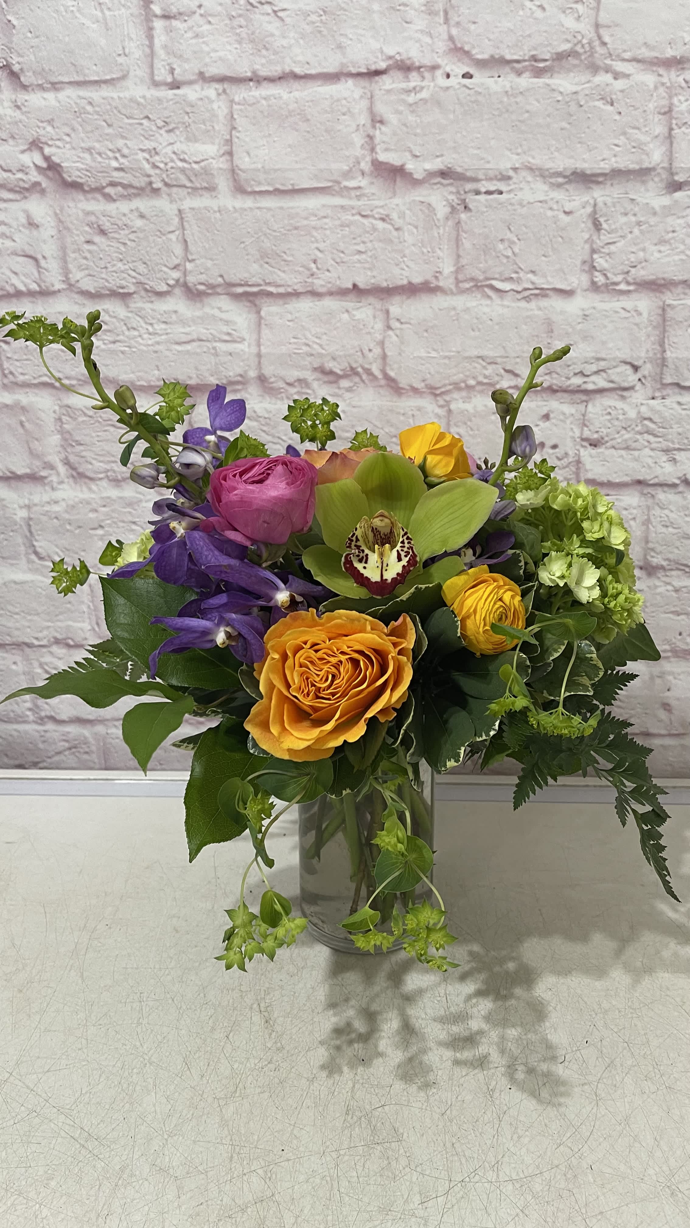 Mixed bouquet in a clear glass vase with orange, pink, purple, and green blooms