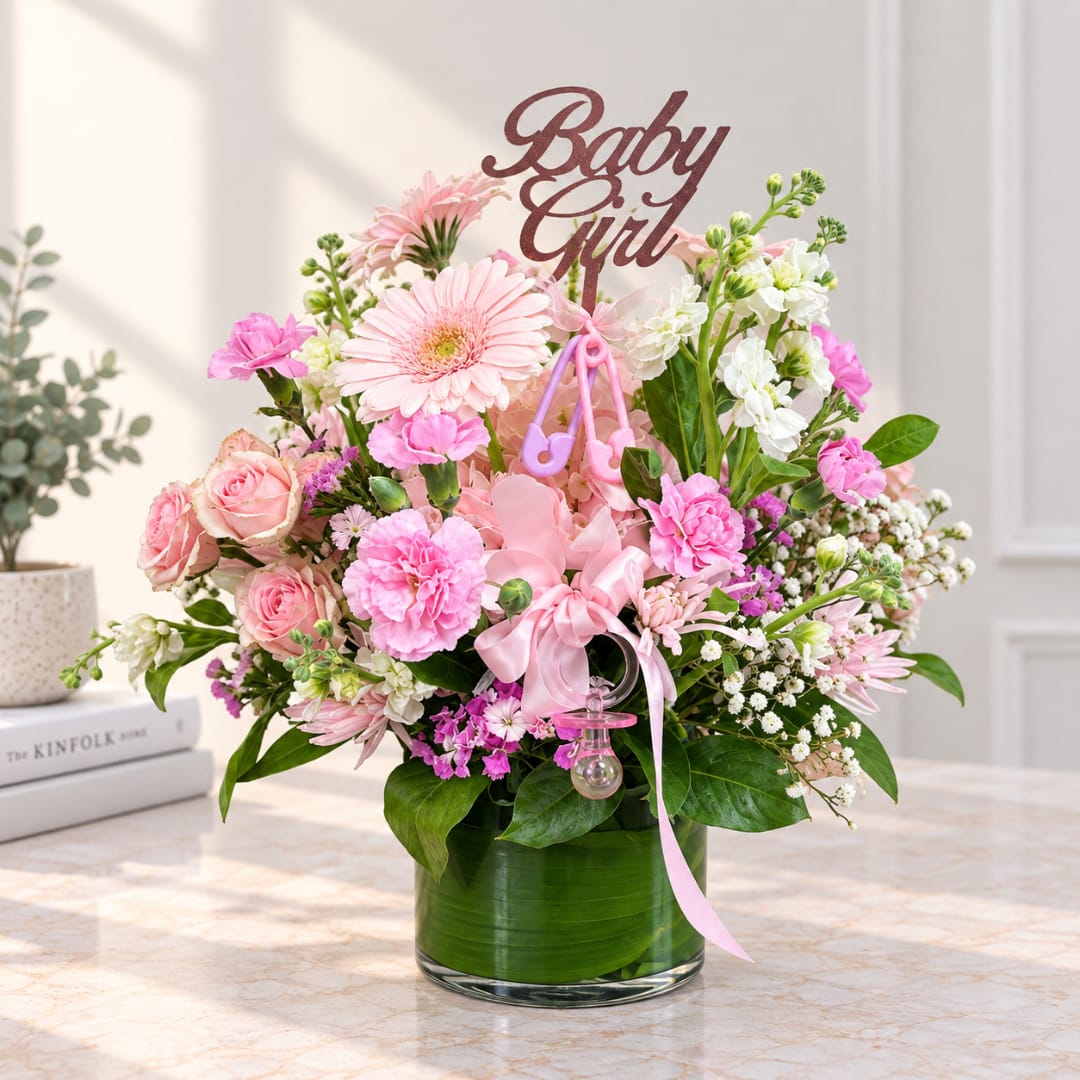 Pink and white floral arrangement in a glass vase with a "Baby Girl" topper