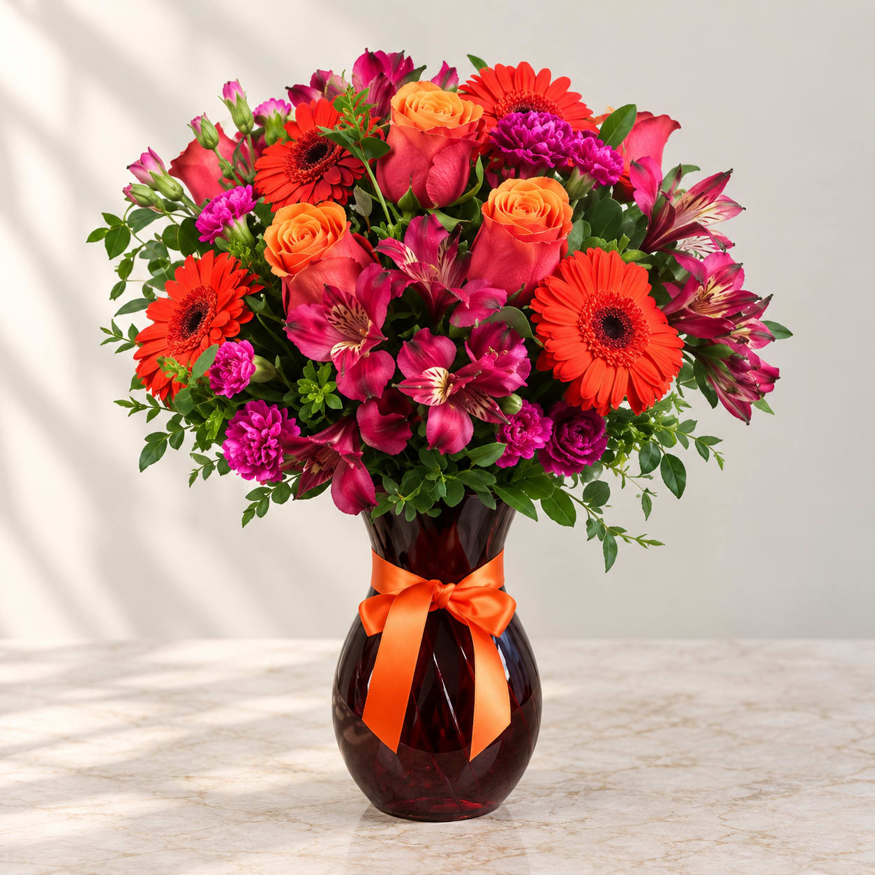 Mixed bouquet of orange, pink, and magenta flowers in a dark glass vase with ribbon