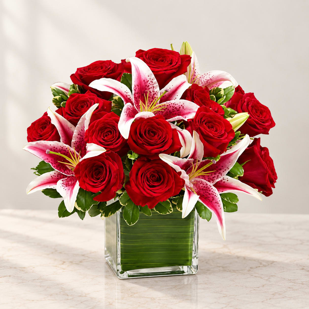 Red roses and pink lilies arranged in a square glass vase