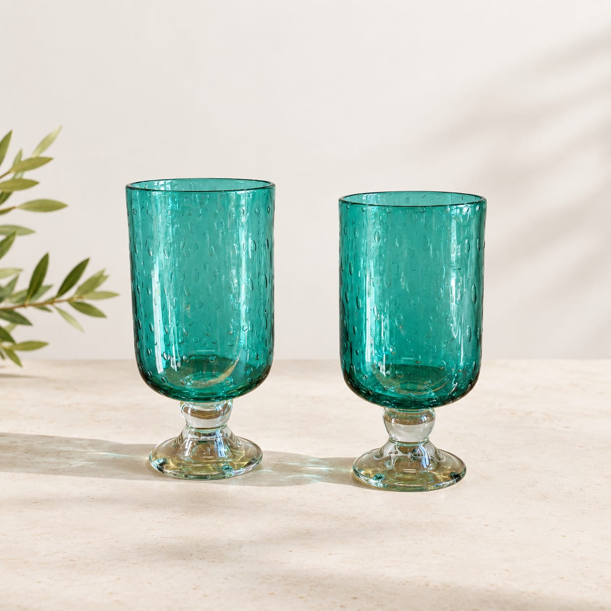 Two teal glass goblets with textured surfaces on a light tabletop