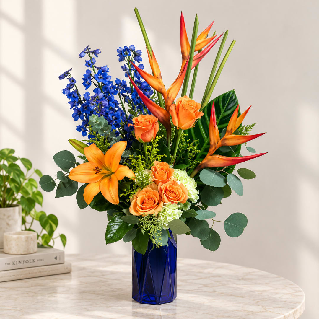 Orange roses, lilies, and blue delphinium in a cobalt vase