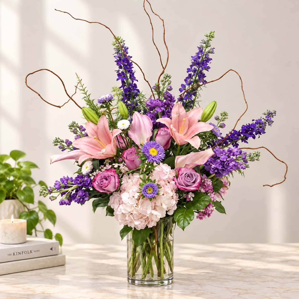 Pink lilies and purple flowers arranged in a clear glass vase