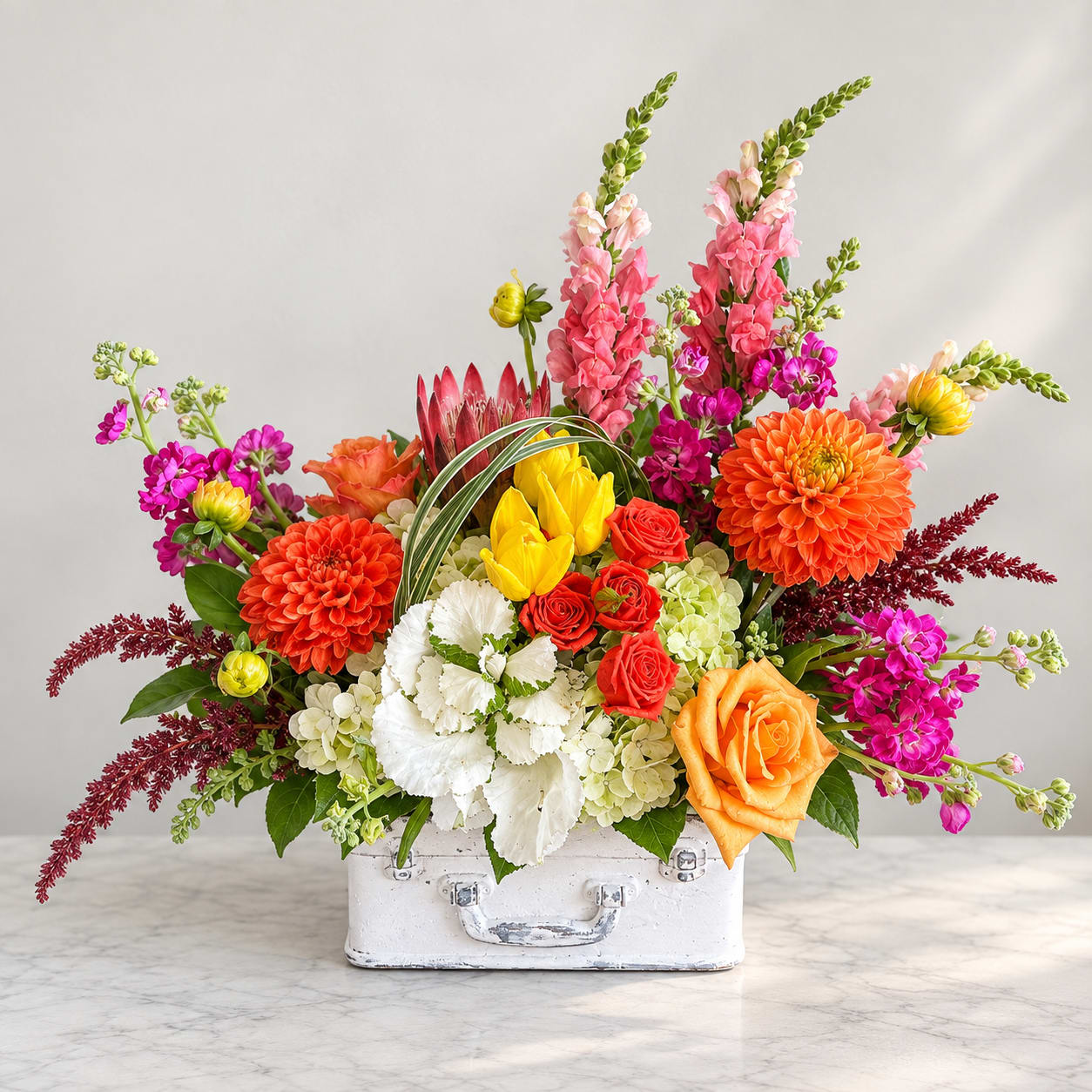 Colorful mixed flower arrangement in a white suitcase-style container