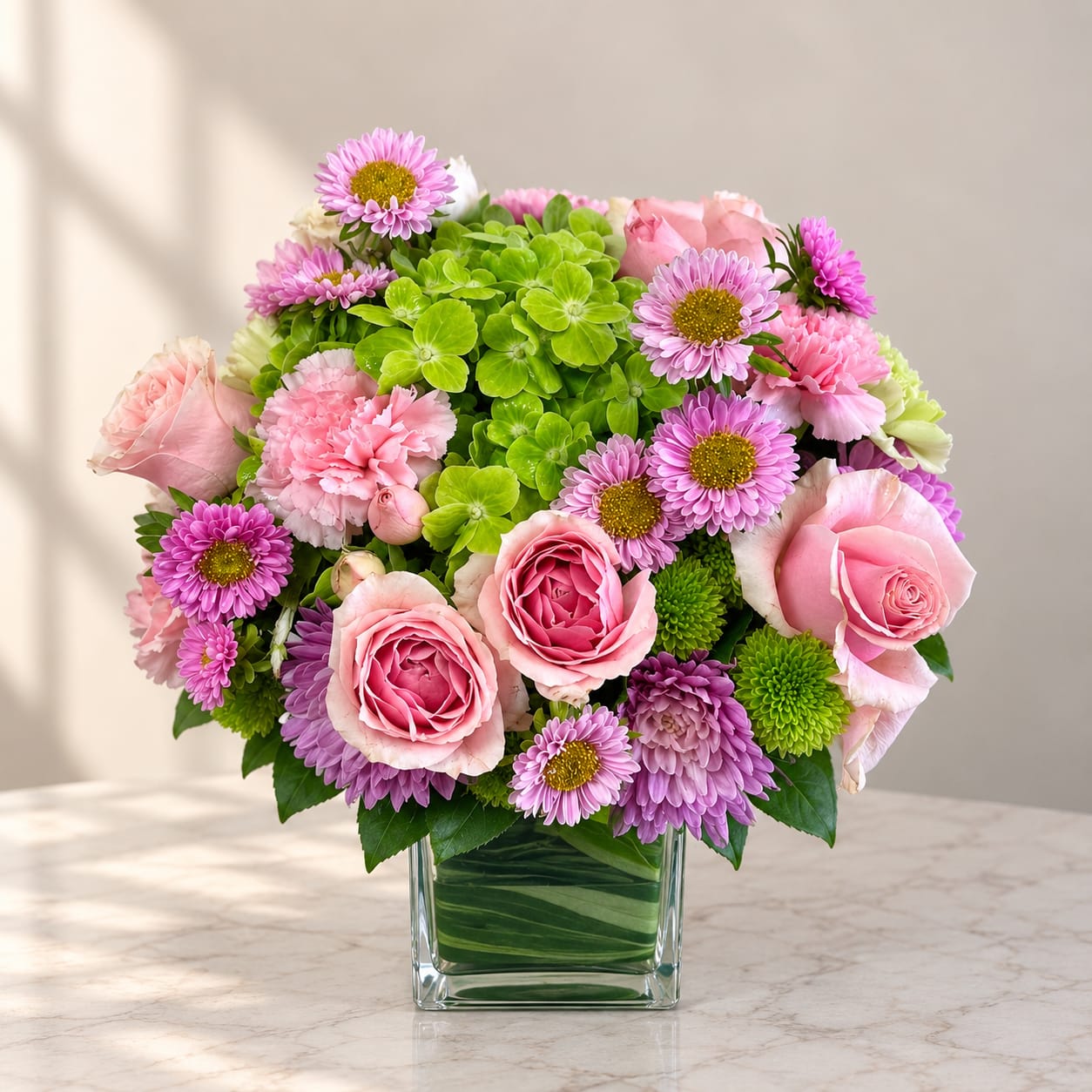Pink roses and purple daisies in a clear square vase