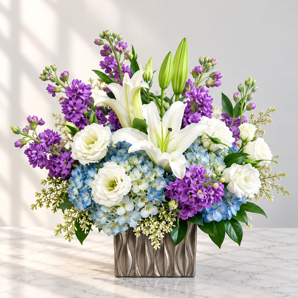 Purple and white floral arrangement with lilies and blue hydrangeas in a metallic vase