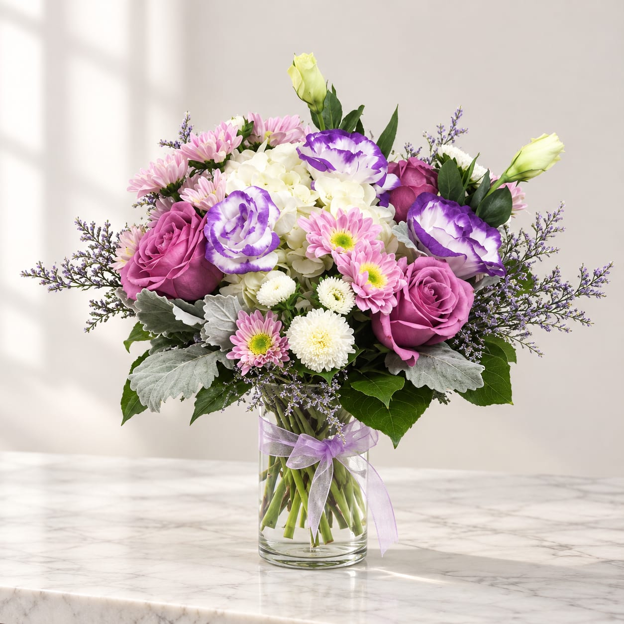Bouquet of pink and purple flowers in a clear glass vase with a ribbon