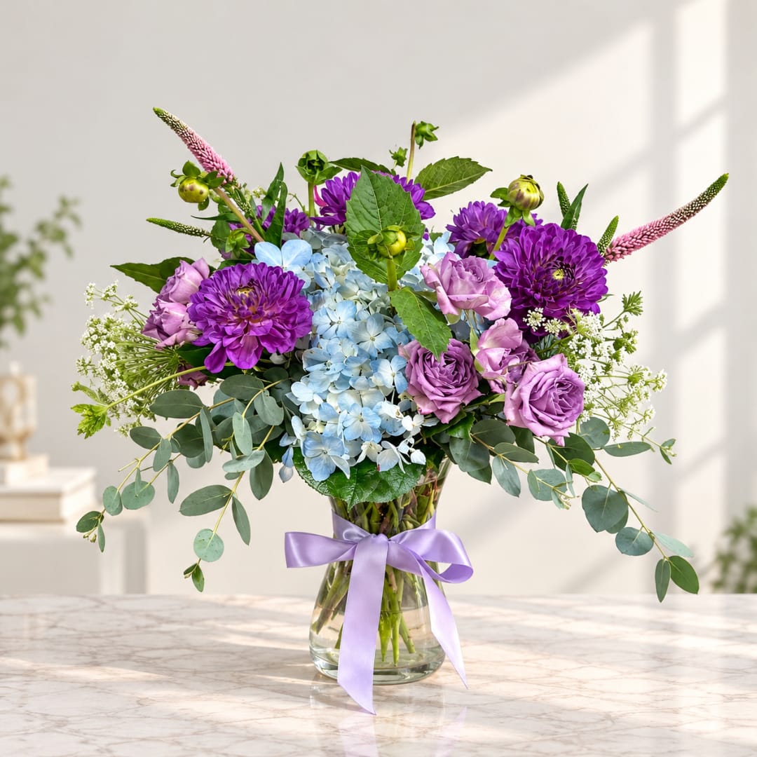 Purple and blue mixed bouquet in a glass vase with a lavender ribbon