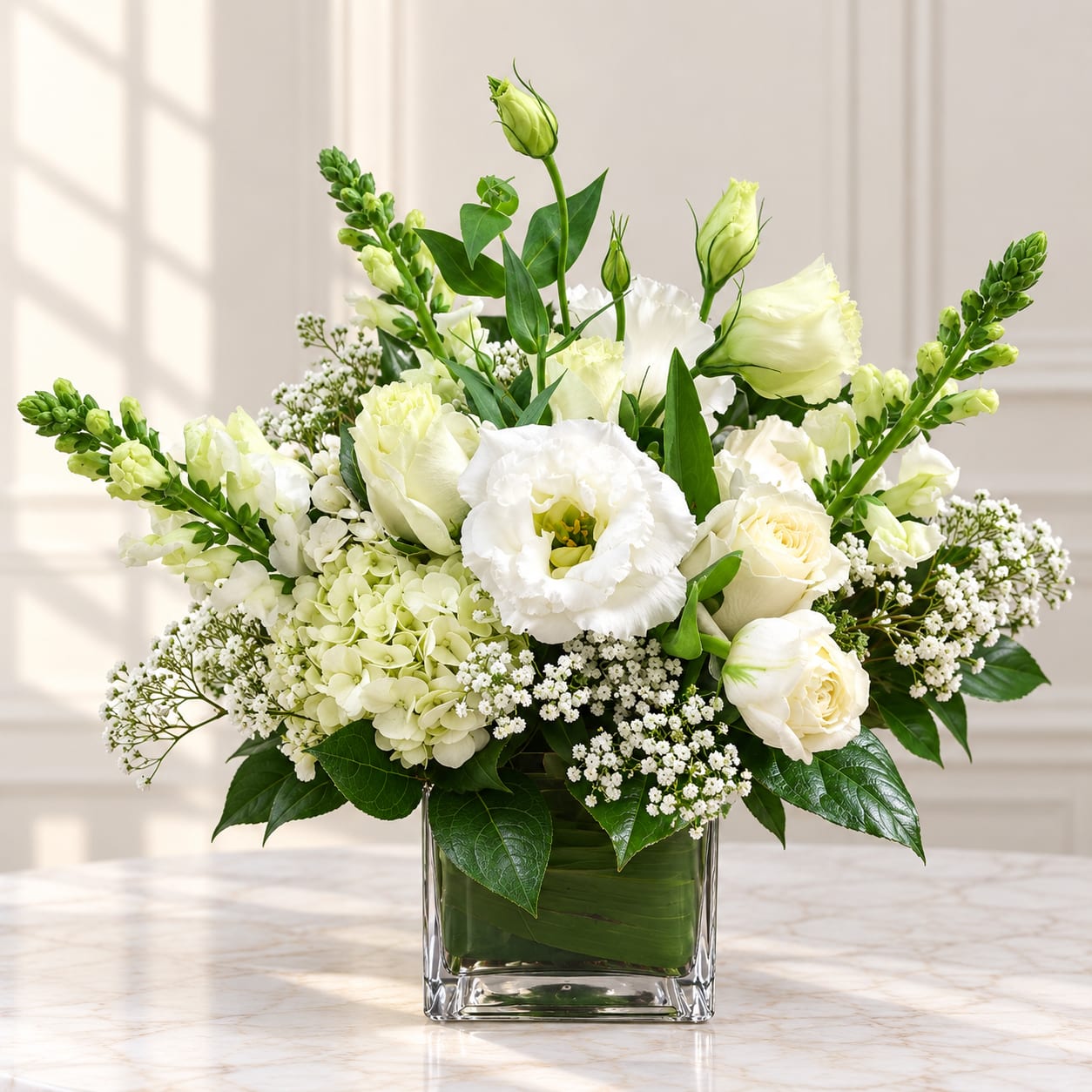 White floral arrangement in a clear square vase with green accents