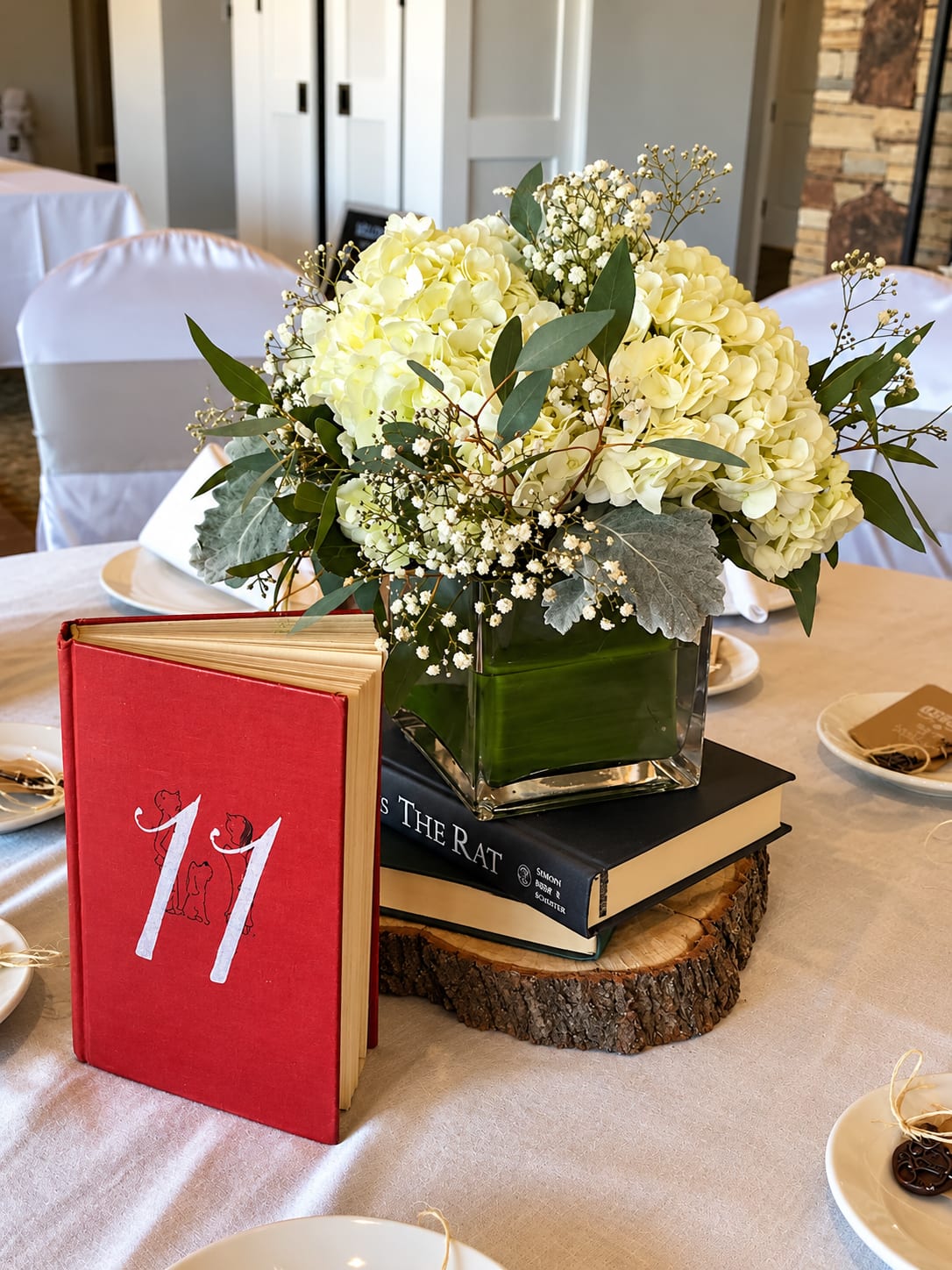 White hydrangea centerpiece in a square glass vase on stacked books