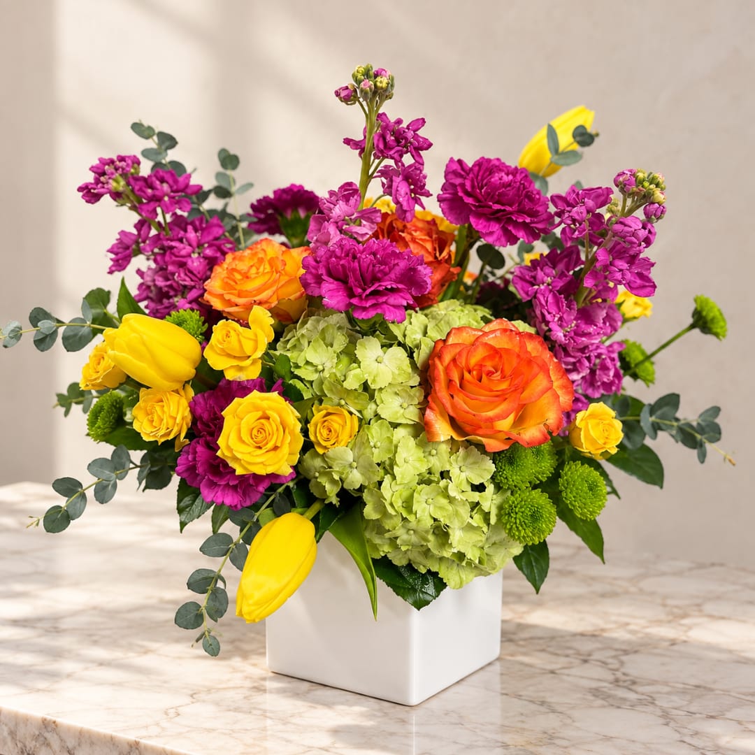 Colorful bouquet in a white square vase with roses, tulips, hydrangea, and purple blooms
