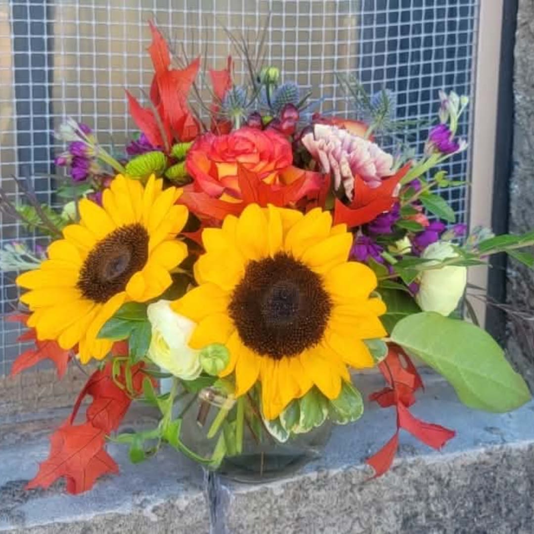 Bright bouquet with sunflowers, roses, and purple accents in a glass vase