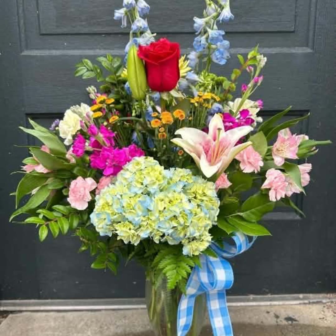 Mixed bouquet in a glass vase with a red rose, lily, hydrangea, and blue ribbon