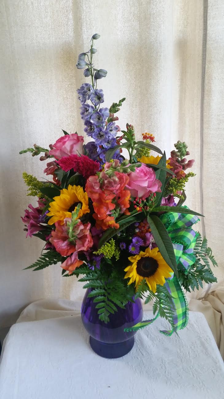 Mixed bouquet in a purple vase with sunflowers, roses, and purple spikes