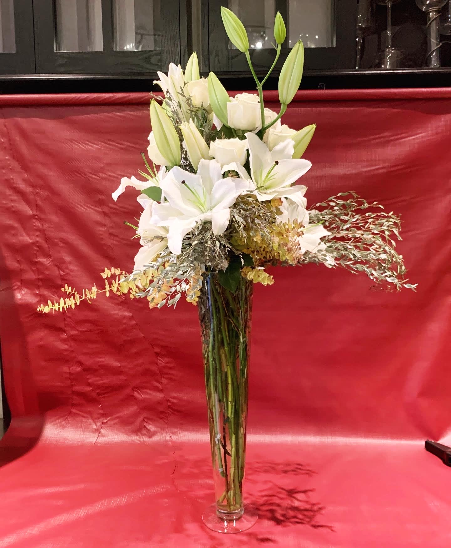 Tall white lily and rose arrangement in a clear glass vase