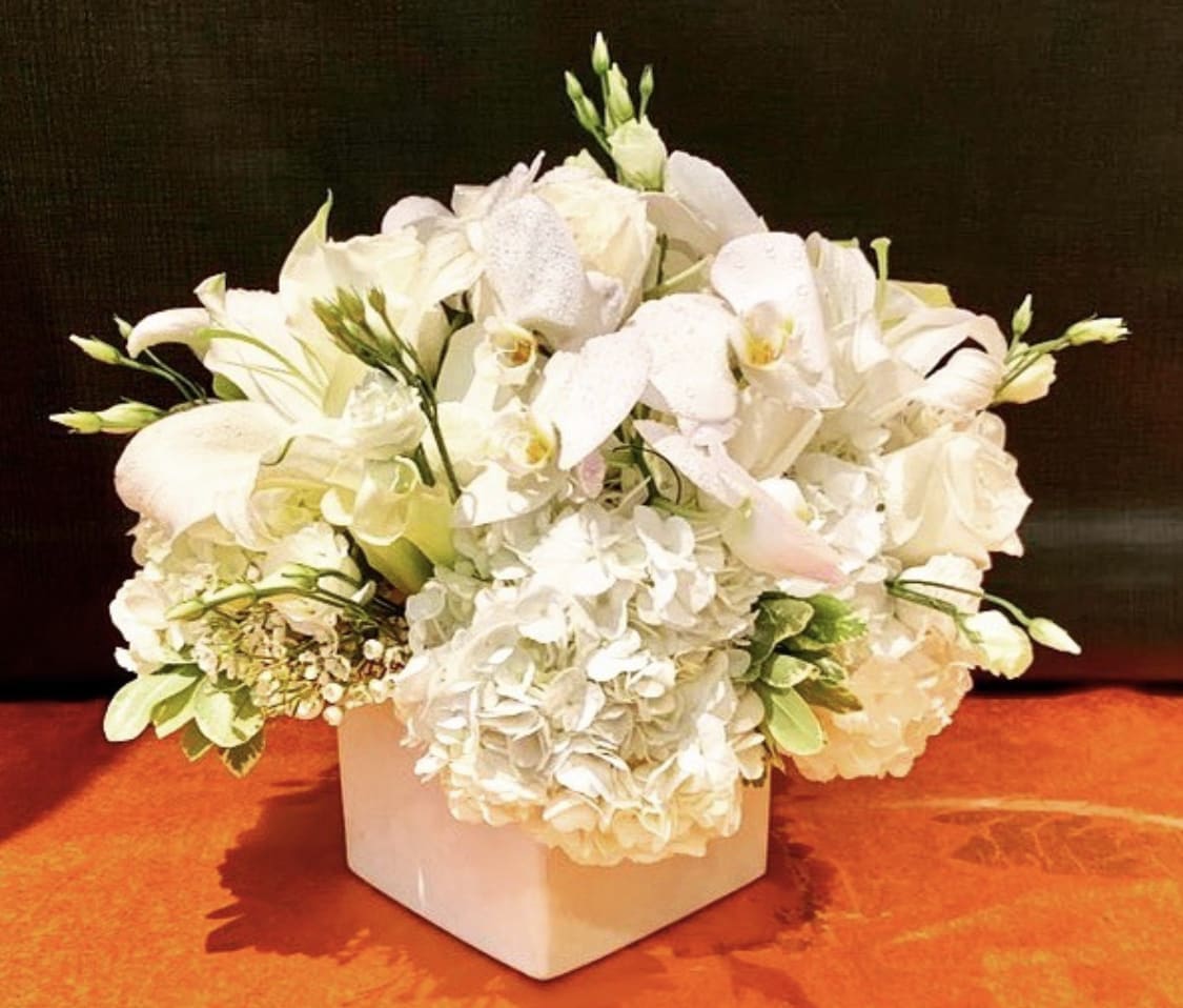 White floral arrangement in a square vase with orchids and hydrangeas