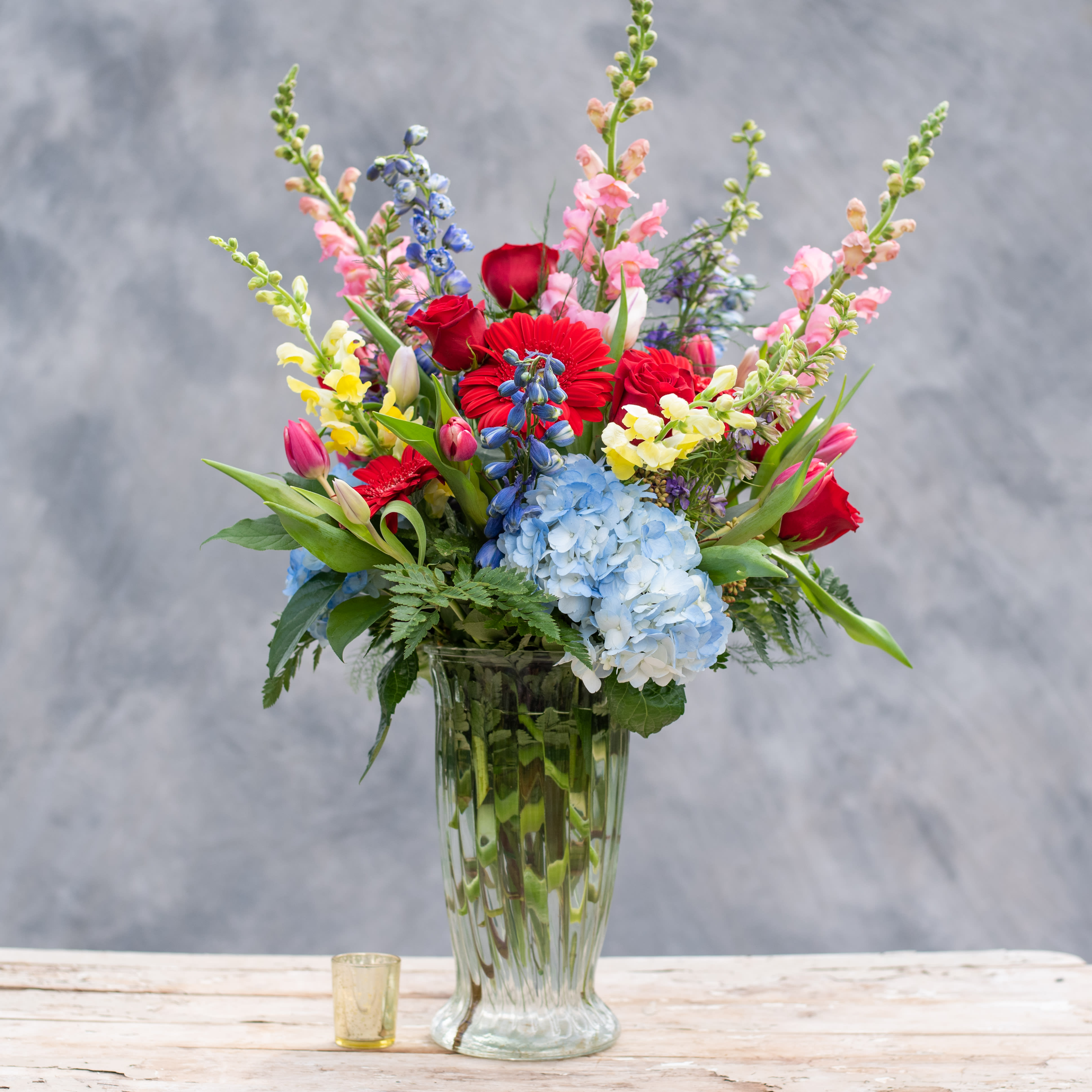 Mixed bouquet in a clear glass vase with red, pink, blue, and yellow flowers