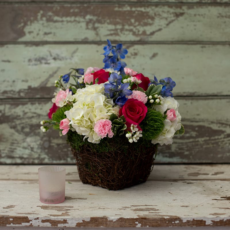 Mixed bouquet in a woven basket with roses, hydrangeas, and blue flowers