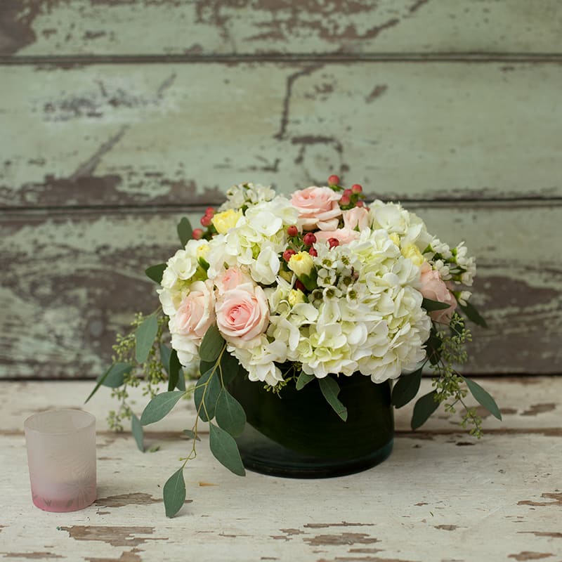 Pink roses and white hydrangeas in a dark vase with a small candle beside it