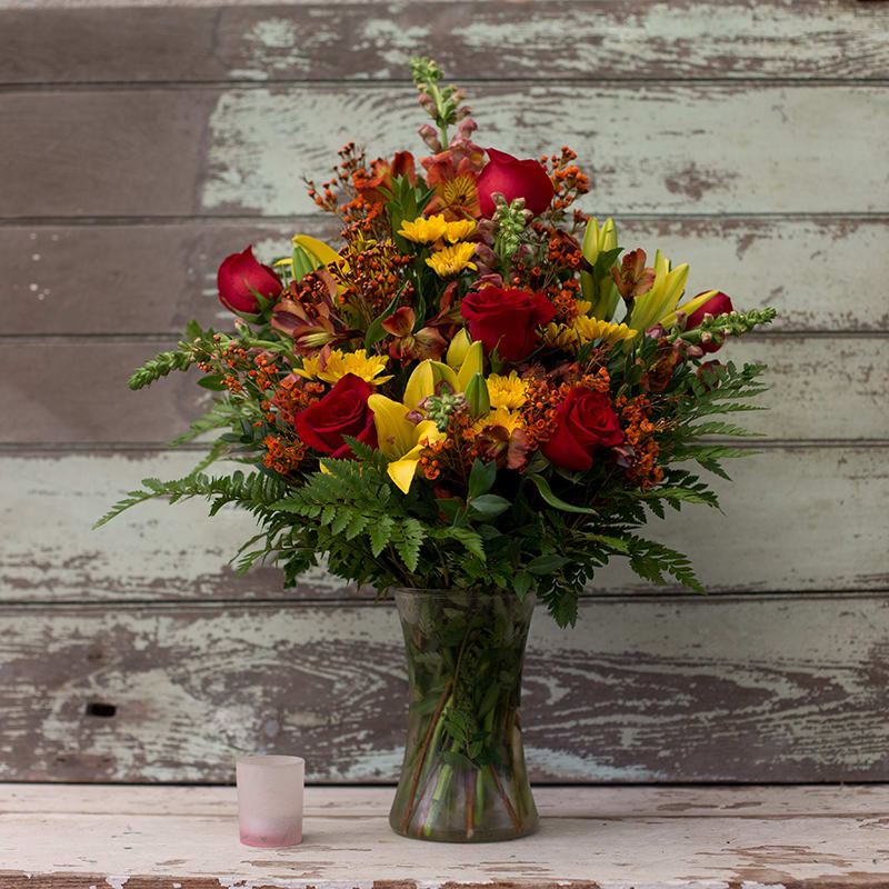 Mixed bouquet of red roses, yellow lilies, and orange flowers in a glass vase