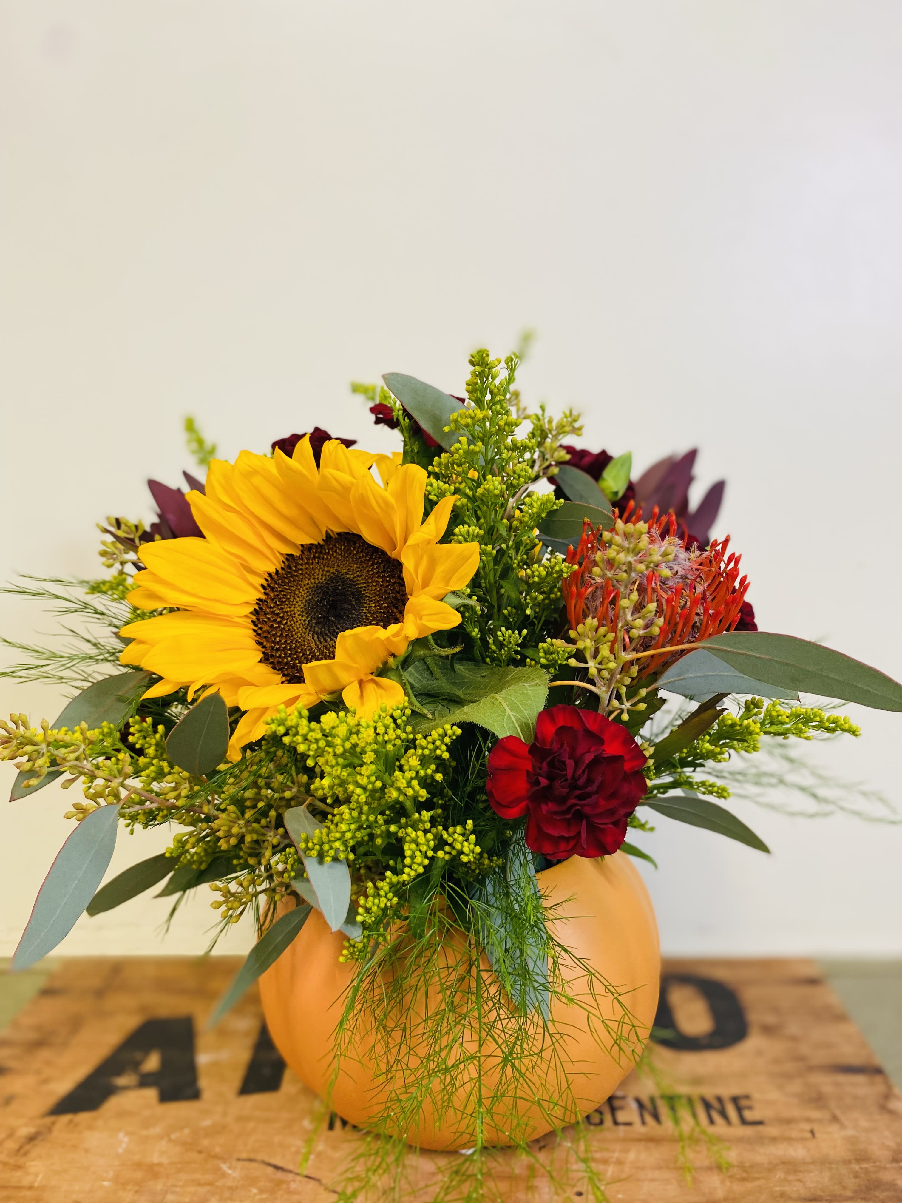 Sunflower and red floral arrangement in an orange pumpkin vase