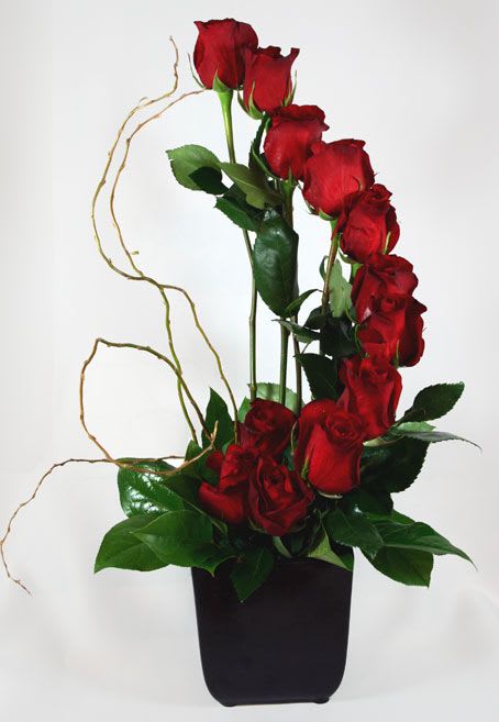 Tall arrangement of red roses in a black vase with curly branches