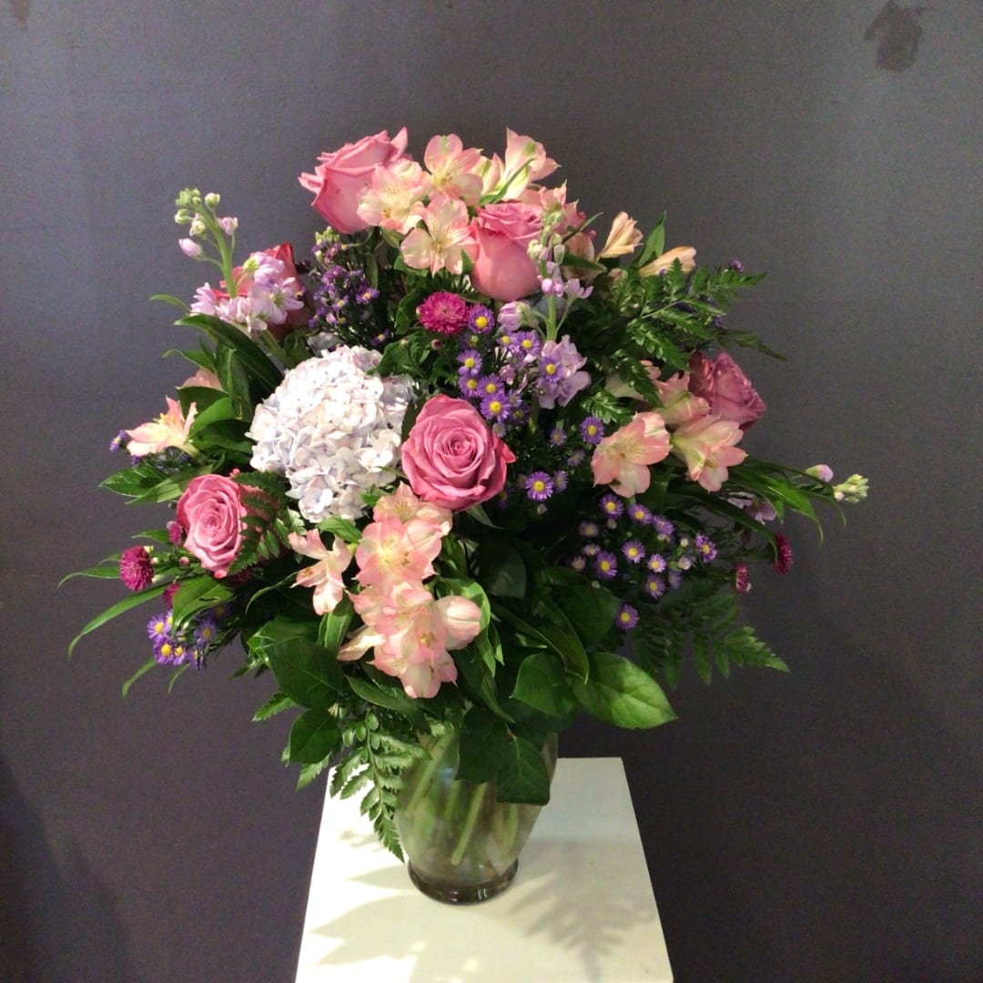 Pink roses and mixed flowers arranged in a clear glass vase