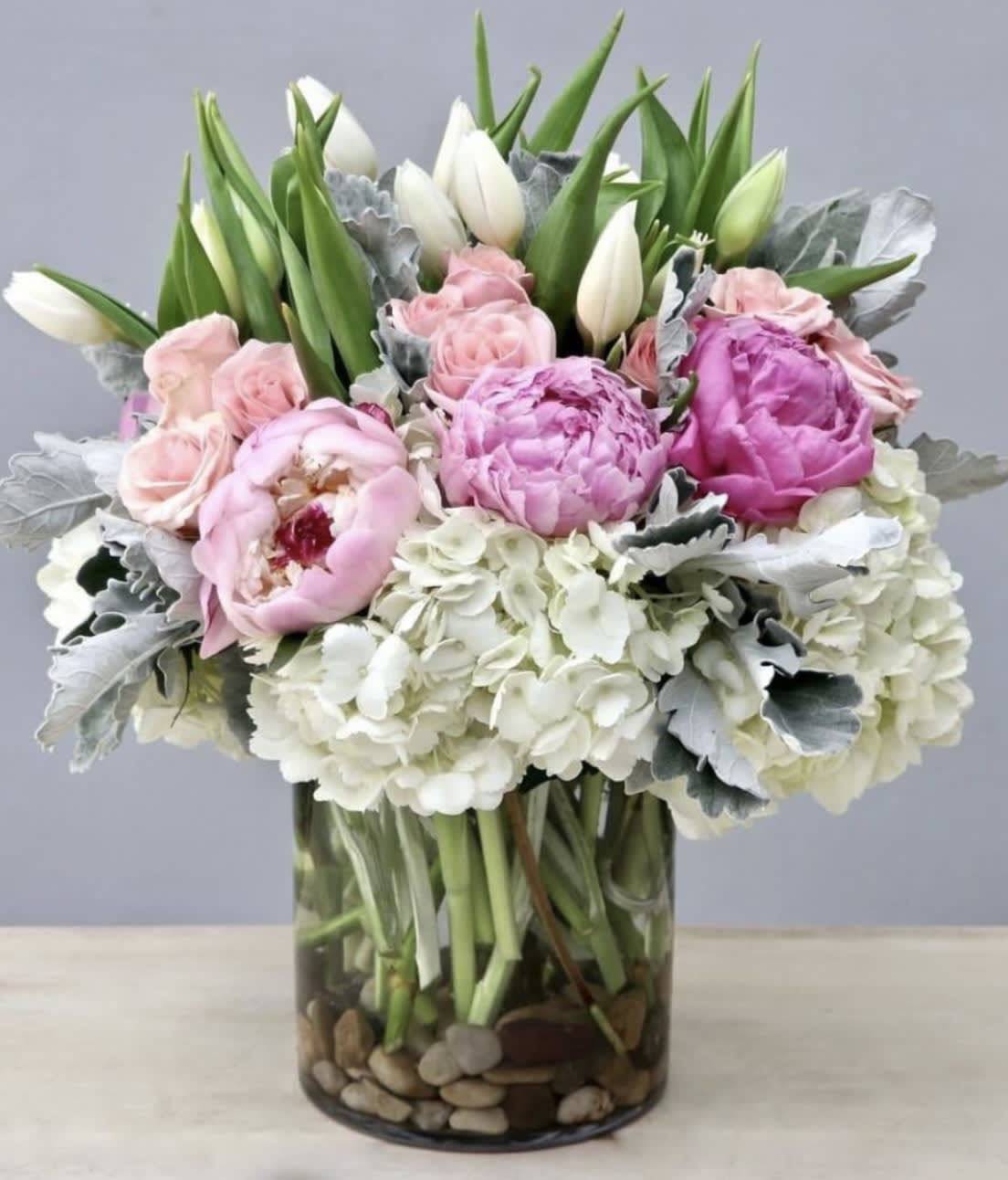 Pink peonies and white tulips in a glass vase with hydrangeas