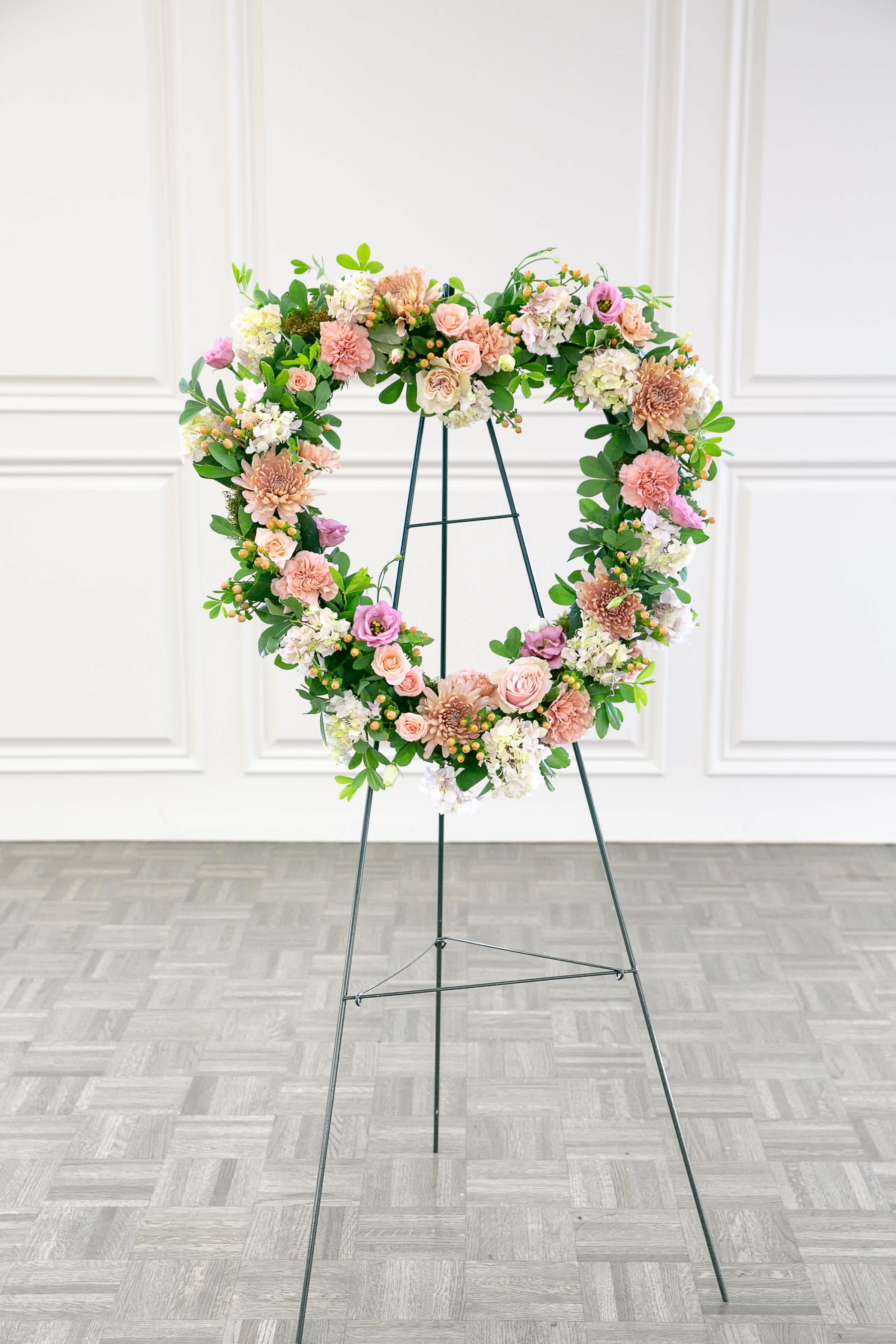 Heart-shaped floral wreath on a metal stand with pink and white blooms
