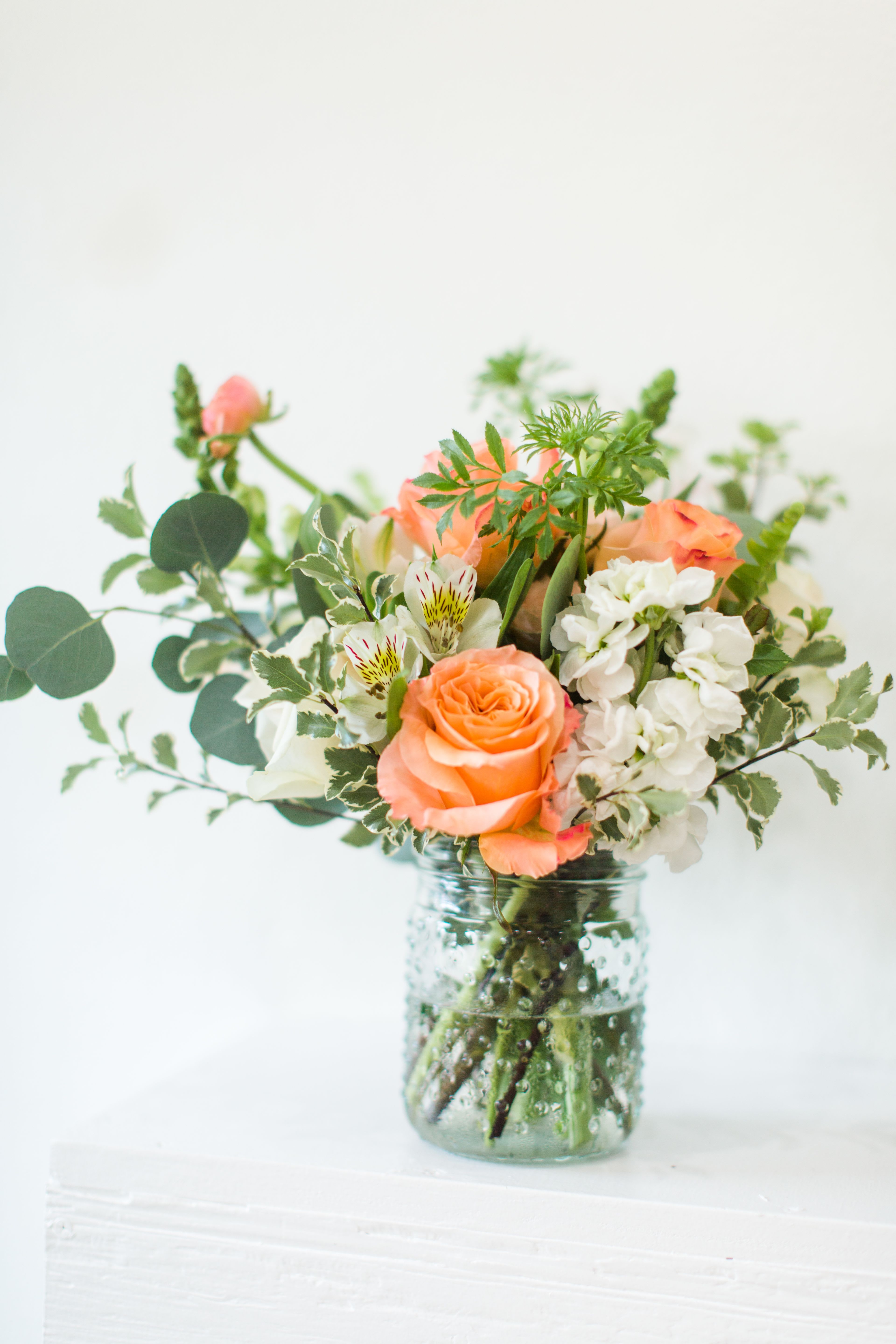 Peach roses and white flowers in a clear glass jar vase