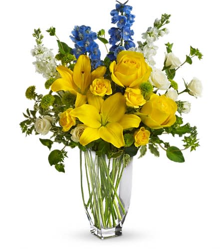 Yellow lilies and roses in a clear glass vase with blue and white flowers