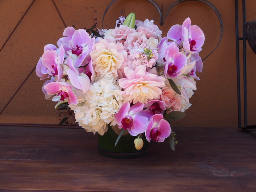 Pink and white orchid arrangement in a dark vase