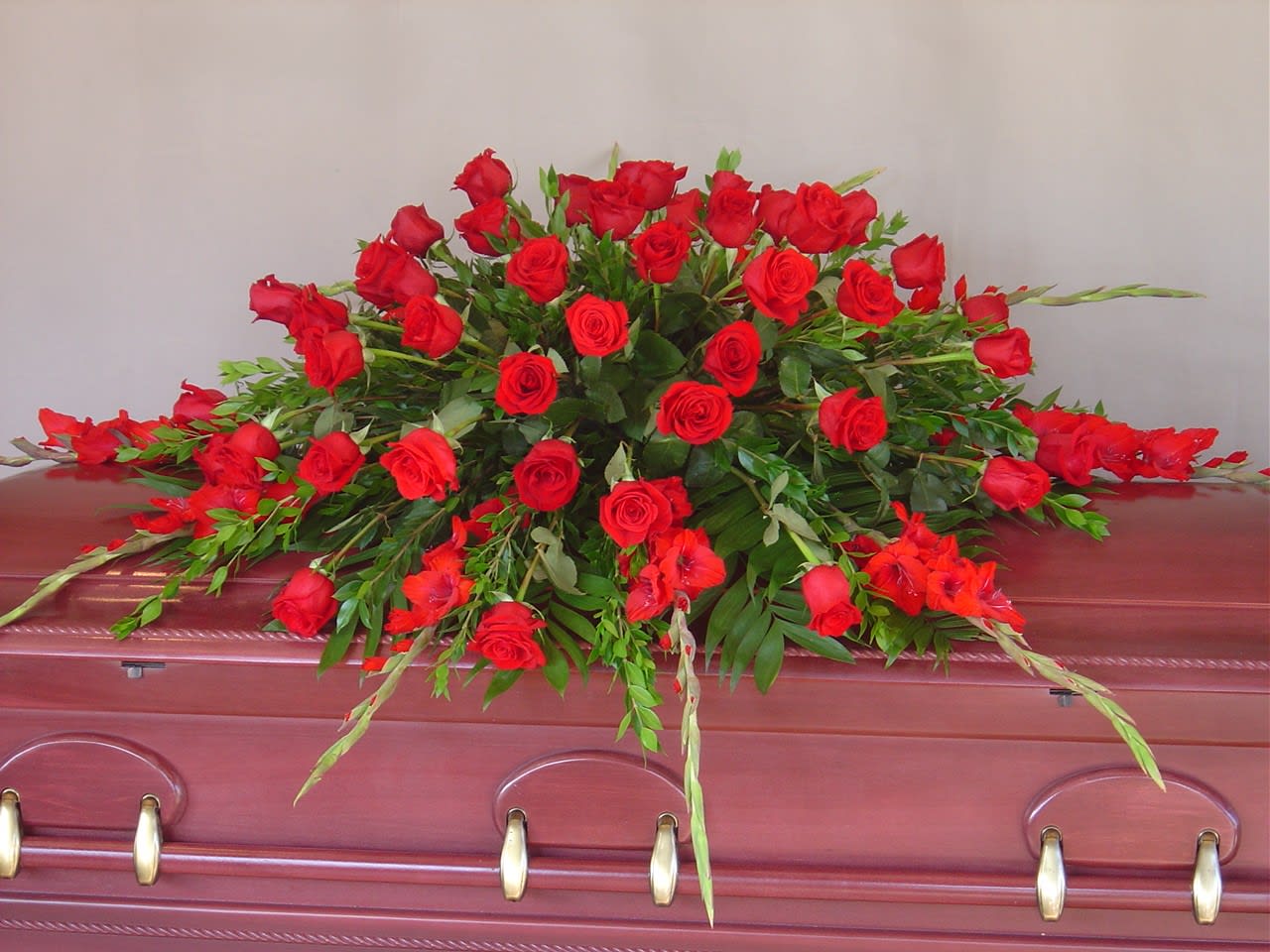 Red rose casket spray with greenery on a burgundy casket