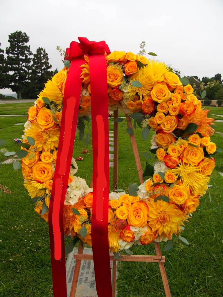 Large floral wreath of yellow and orange roses with a red ribbon