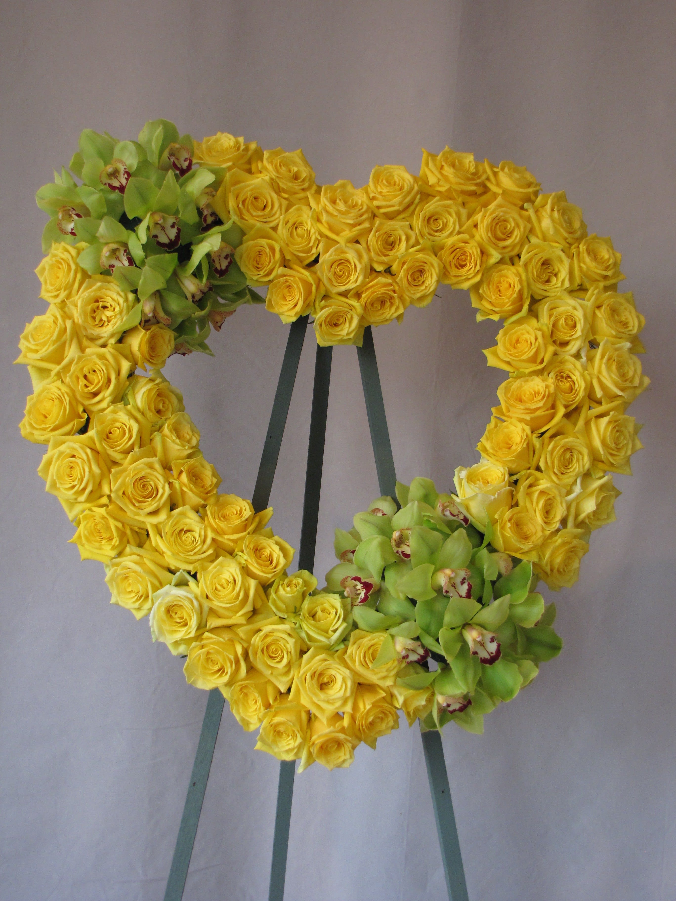 Heart-shaped wreath of yellow roses with green orchids on an easel