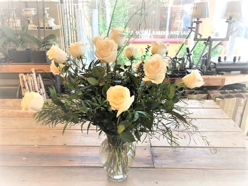 Cream roses arranged in a clear glass vase with airy greenery.