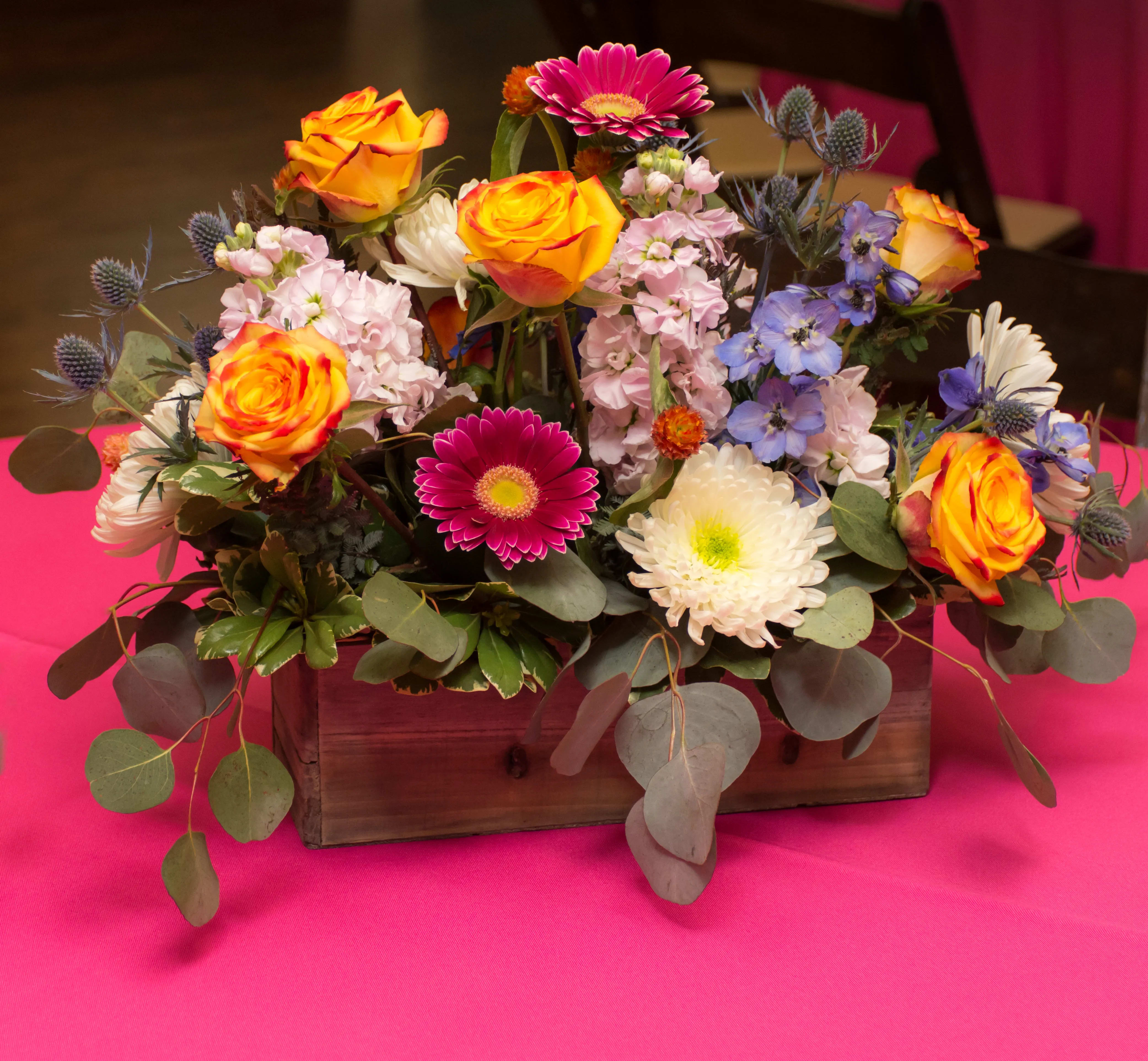 Mixed bouquet in a wooden box with orange roses and pink, white, and blue flowers