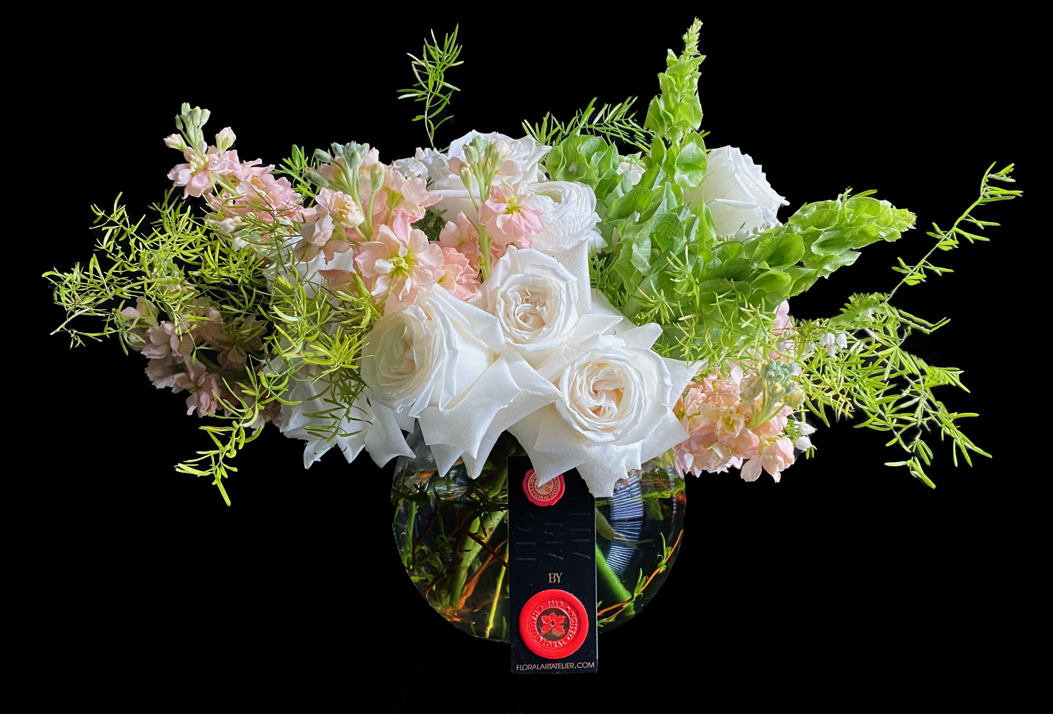 Low round arrangement of white roses and soft pink flowers in a clear bowl vase with airy greenery.