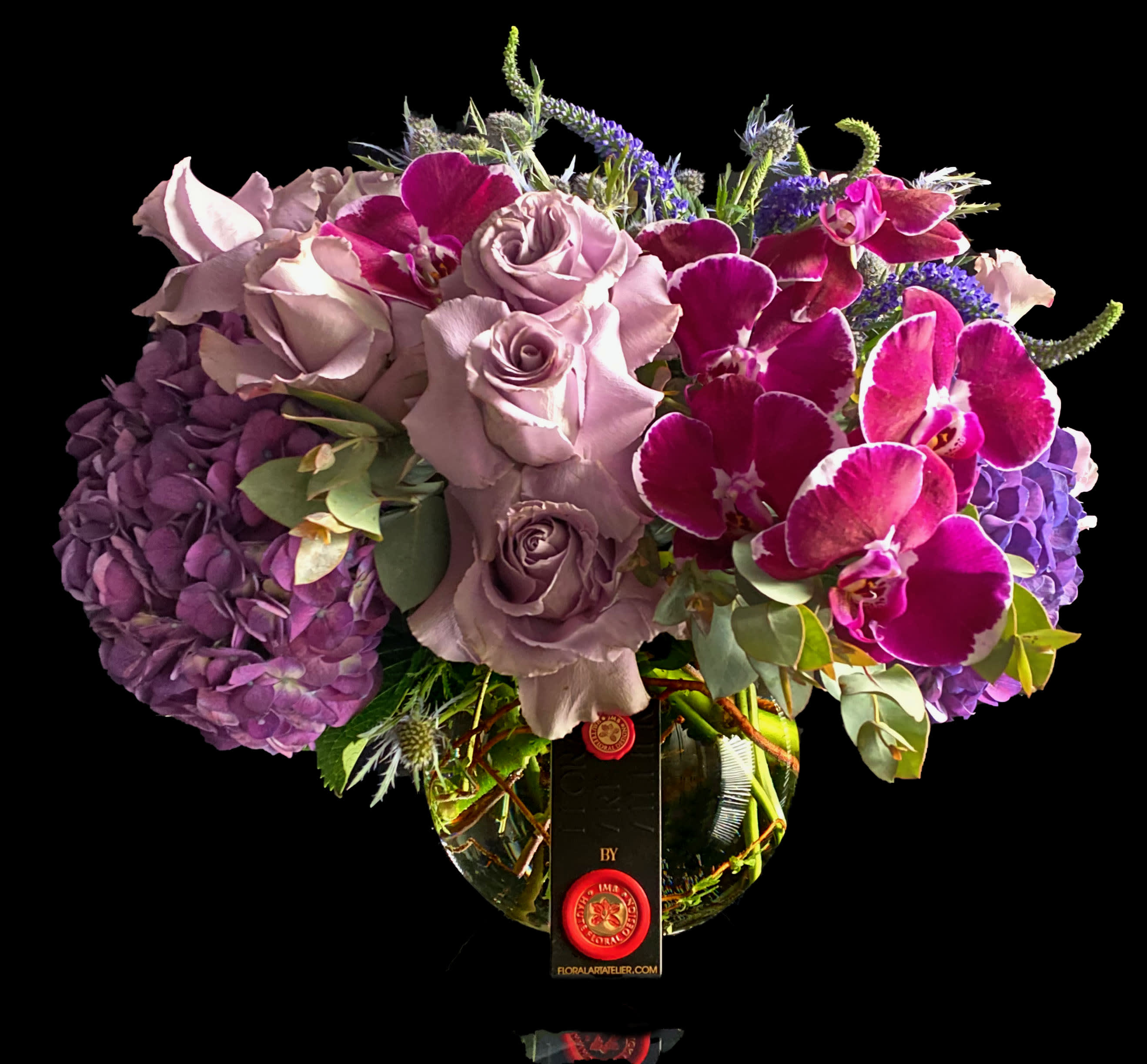 Bouquet of lavender roses, purple hydrangeas, and magenta orchids in a glass vase