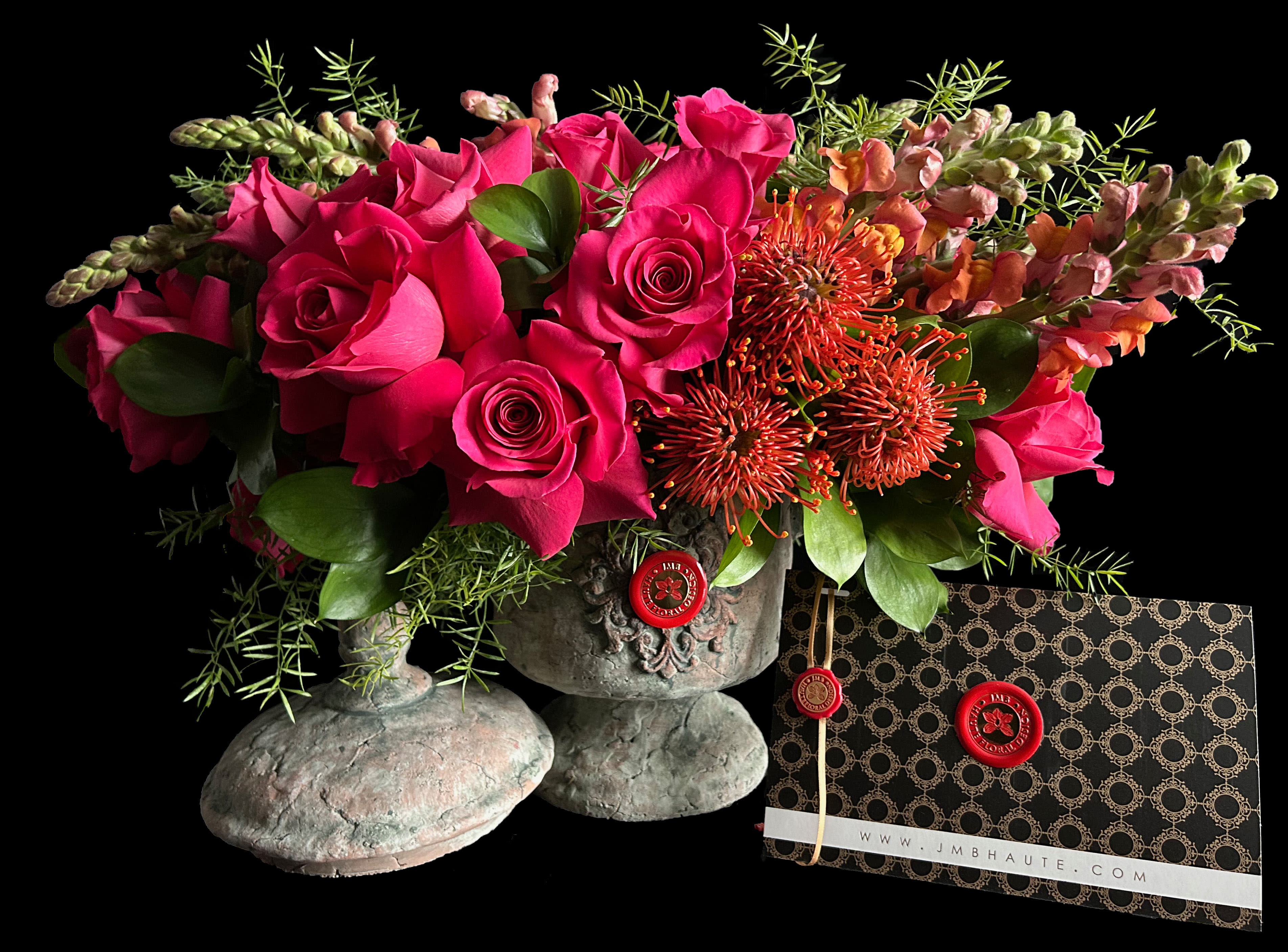 Hot pink roses and orange pincushion blooms in a stone vase with a patterned card
