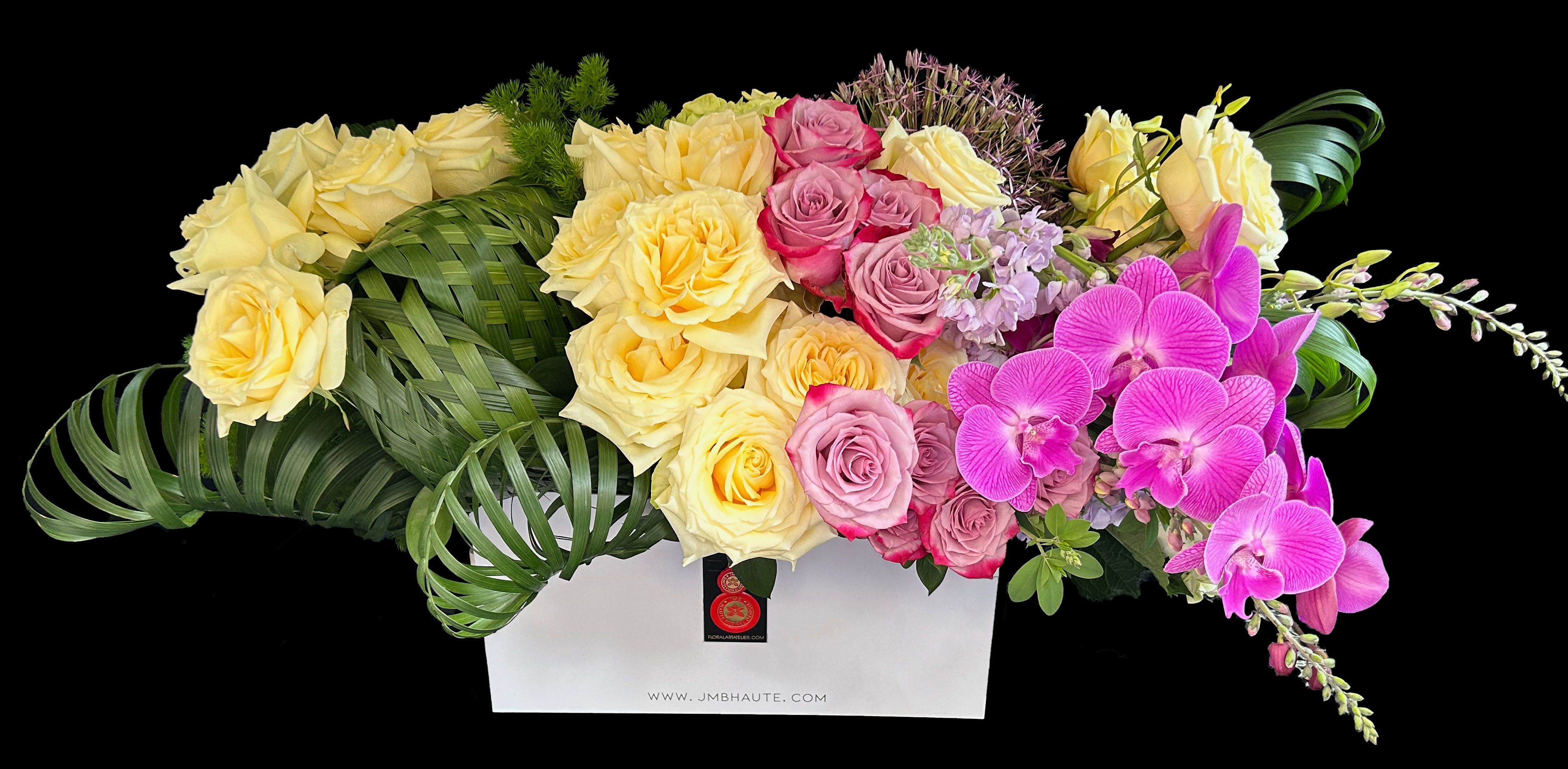 Nautilus - Elaborate floral composition inspired in the nautilus mollusk with a light external spiral shell, it symbolizes growth , expansion and renewal. Roses, dendrobium and phalaenopsis orchids , agapanthus or allium, weaved palm, stock and variegated foliage in  15 in long rectangular vase. 